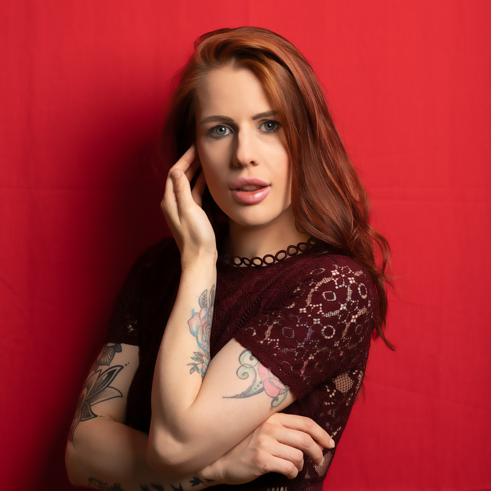 Female model with auburn hair and tatoos against a red backdrop